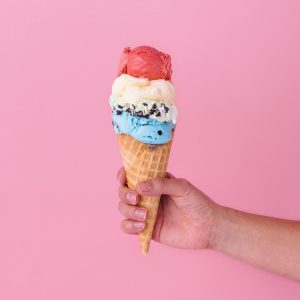 cone with 4 scoops of ice cream being held by one hand against a pink background